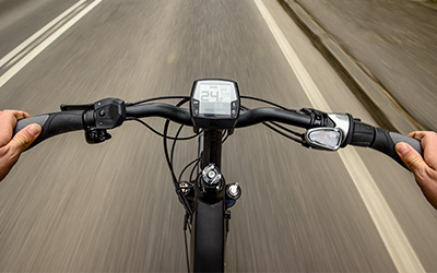 Fahrradlenker von einem eBike mit Tacho und Straße mit Bewegungsunschärfe